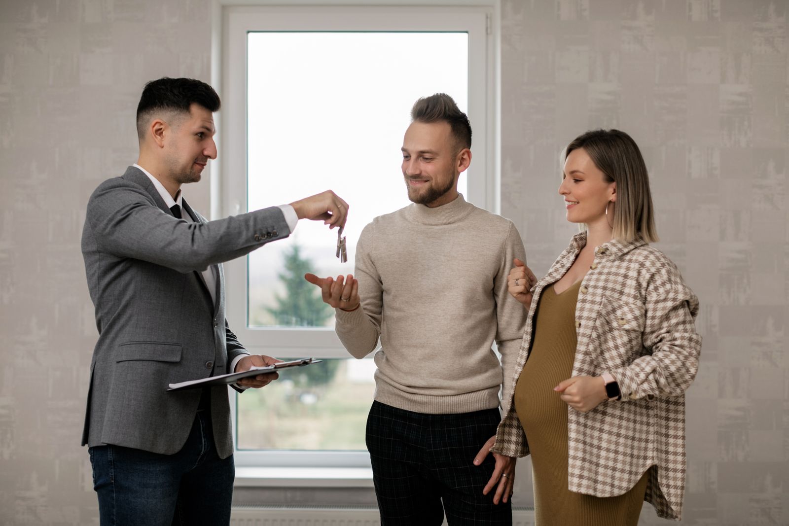 Real estate agent handing house keys to a smiling couple in a bright finished interior